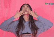 a woman is standing in front of a pink wall with her arms outstretched .