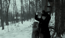 a woman in a black coat is standing in the snow next to a tree