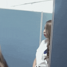 a woman is standing in front of a blue wall and looking at herself in the mirror