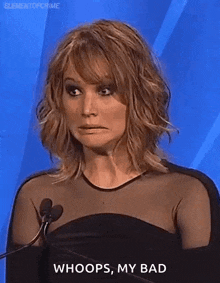 a woman is making a funny face while standing in front of a microphone and saying whoops , my bad .