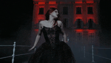 a woman in a black dress stands in front of a building with red lights on it