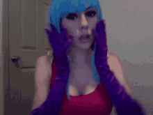 a woman with blue hair and purple gloves looks at the camera