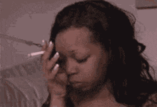 a woman is smoking a cigarette and holding her hand to her head .
