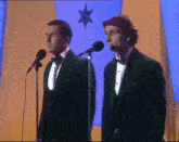 two men in tuxedos standing in front of microphones