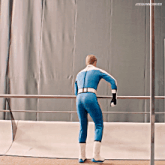 a man in a blue suit and white boots leans against a railing