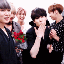 a group of young men standing next to each other with one man holding a bouquet of red roses