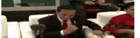 a man in a suit and tie is sitting in front of a microphone and giving a thumbs up .
