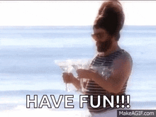 a man with a beard is holding a martini on the beach with the words have fun written below him