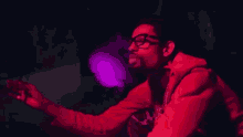 a man wearing glasses and a red jacket is smoking a cigarette in a dark room .