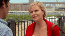 a woman in a red jacket talks to a man in a blue shirt