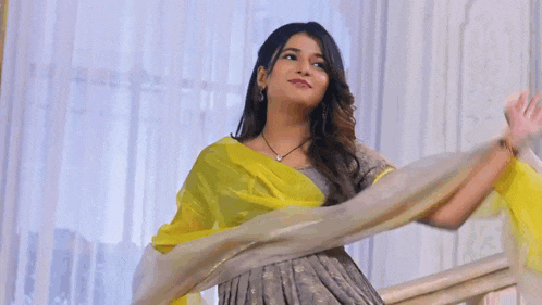 a woman in a grey dress with a yellow dupatta is dancing .