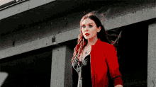 a woman wearing a red jacket is standing in front of a building