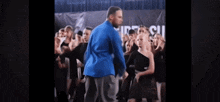 a man in a blue shirt is standing in front of a group of young dancers .