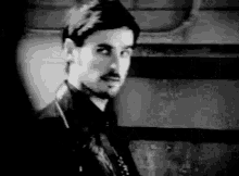 a man with a beard is wearing a leather jacket and looking at the camera in a black and white photo .