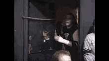 a man in a black tank top is standing in a dark room talking to a group of people .