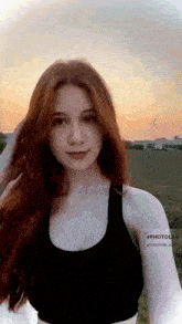 a woman with red hair is wearing a black sports bra and looking at the camera .