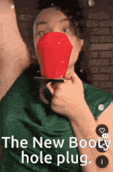 a woman wearing a green shirt is holding a red object in front of her face ..