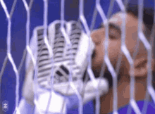 a soccer goalie is drinking water from a bottle through a soccer net .