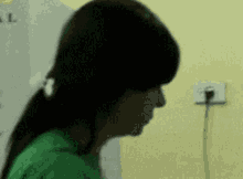 a woman wearing a green shirt is standing in front of a wall with a plug in it .