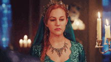 a woman in a green dress with a tiara on her head stands in front of candles