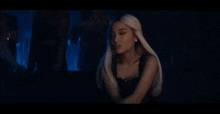 ariana grande is sitting on a couch in a dark room in a black dress .