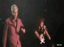 a man in a pink suit is dancing next to a woman in a red dress who is singing into a microphone