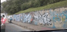 a car is driving past a wall that has graffiti on it including the word " nasty "