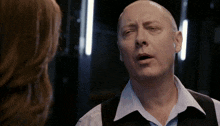 a man in a vest and striped shirt is talking to a woman in a dark room