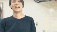 a man in a black shirt is smiling in front of a white wall