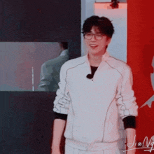 a man wearing glasses is standing in front of a red wall and smiling .
