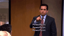 a man in a suit and tie is pointing at the camera with the words " powerpoint " on the screen behind him
