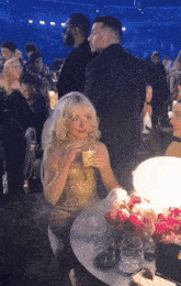 a woman in a gold dress sits at a table with glasses of wine