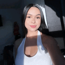 a woman in a white tank top is taking a selfie with the sun shining on her