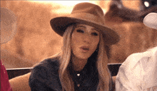 a woman wearing a hat and a denim shirt is sitting in a car