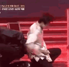 a man in a white shirt is kneeling down on a stage with a red light behind him .