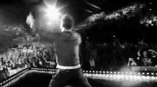 a black and white photo of a man standing on a stage in front of a crowd .