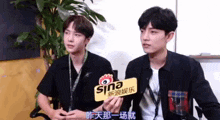 two young men are sitting next to each other in front of a plant .