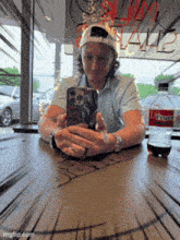 a man sits at a table looking at his phone next to a bottle of diet dr pepper