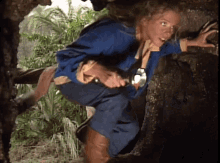 a woman in a blue jacket is crawling through a hole in a tree