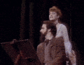 a woman is sitting on a man 's shoulders while he looks at a piece of paper
