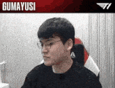 a man wearing glasses is sitting in a chair with the name gumayusi on the top