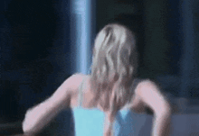 a woman in a blue tank top is standing in front of a window in a dark room .
