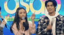 a man and a woman are standing next to each other on a stage holding microphones .