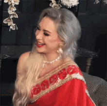 a woman is wearing a red and gold embroidered saree and smiling .