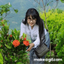 a woman with glasses is standing next to a bush with orange flowers ..
