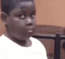 a young boy in a white shirt is making a funny face and looking at the camera .