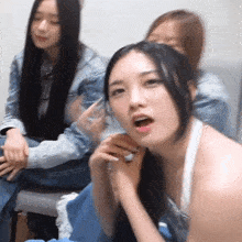 a group of young women are sitting on a couch and one of them is wearing a white tank top .