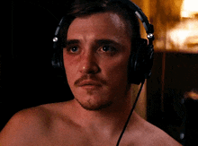 a shirtless man with a mustache is wearing headphones and making a funny face .