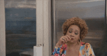 a woman with curly hair is sitting in front of a refrigerator and eating a piece of food .