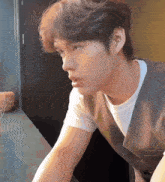 a young man wearing a white shirt and a brown vest is sitting at a table